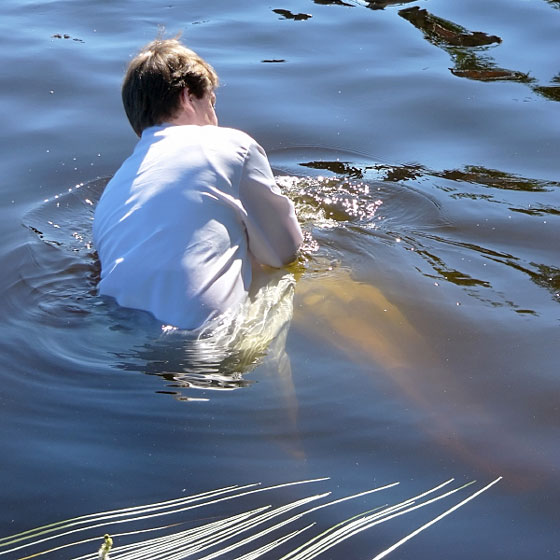 a pastor baptizing a believer in a lake, by immersion